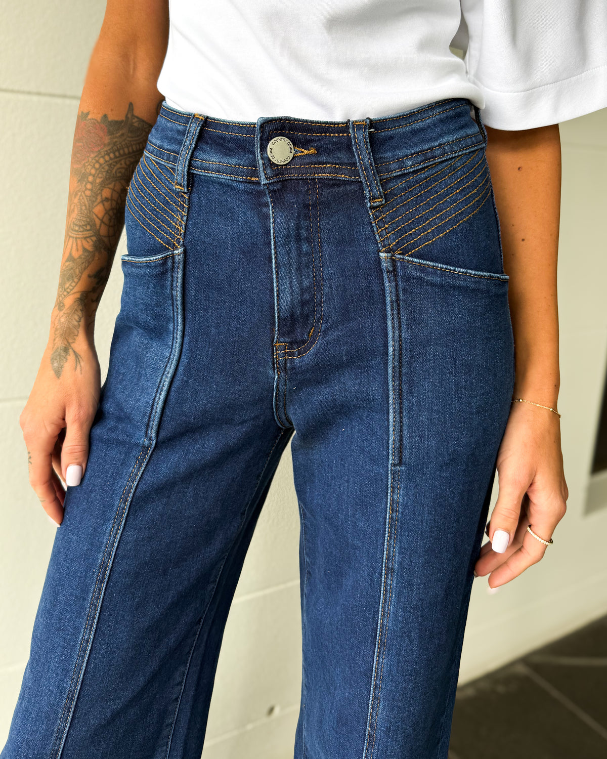 Person wearing blue jeans with a white shirt, standing against a neutral background